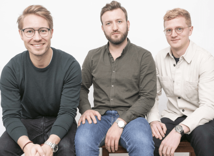 Three men sit in a row against a white background.