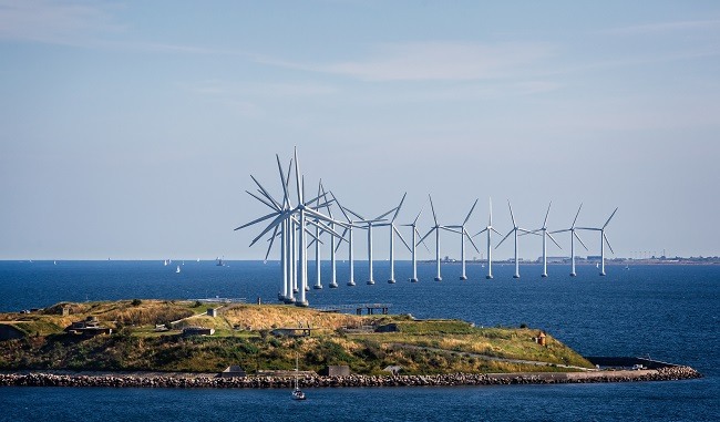 More than a dozen offshore wind turbines in a row beside a small island.