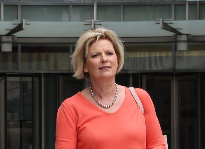 A blonde woman in an orange top and carrying a handbag exits the offices of the BBC in London.