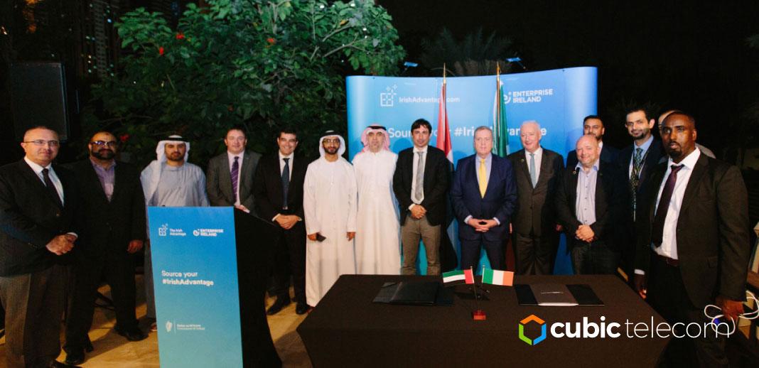 A large group of men in black suits and white outfits. Some are wearing traditional UAE ghutras. Behind them is a blue Enterprise Ireland sign. 