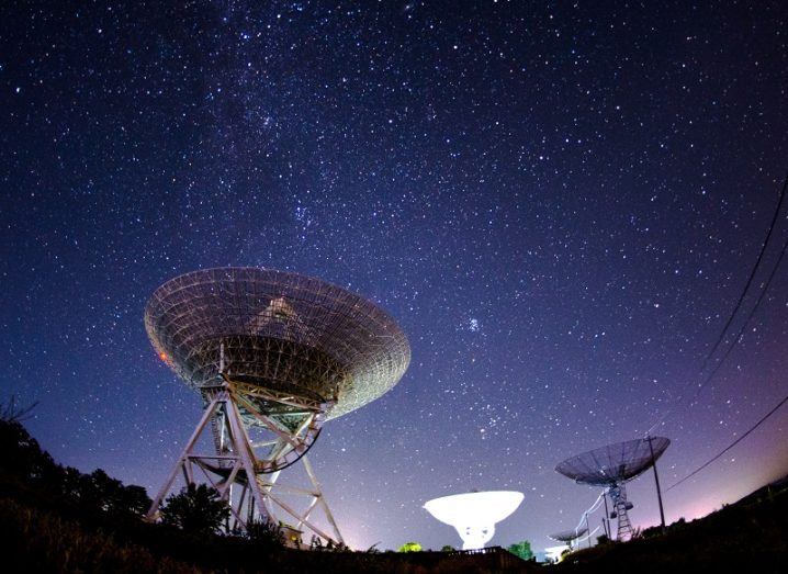 Fisheye lens shot of radio telescopes pointed at the Milky Way at night.