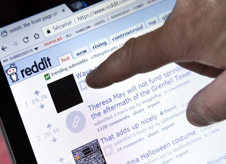 Person's finger pointing at the front page of Reddit on a computer screen.