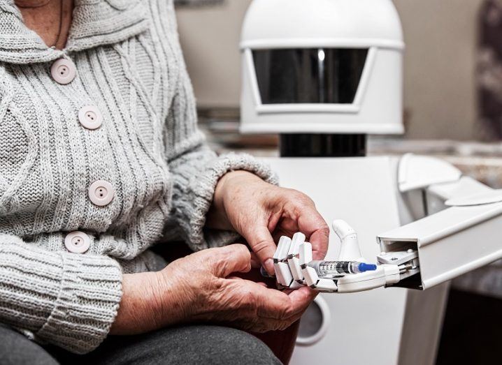 Healthcare robot assisting an elderly person wearing a cardigan.