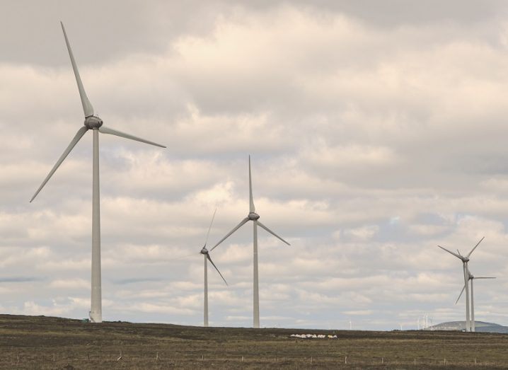 Field of five wind turbines against a grey sky.