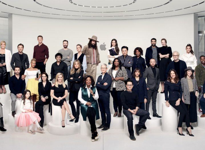A group of famous faces sitting and standing in front of a white screen at the launch of the Apple TV+ service.