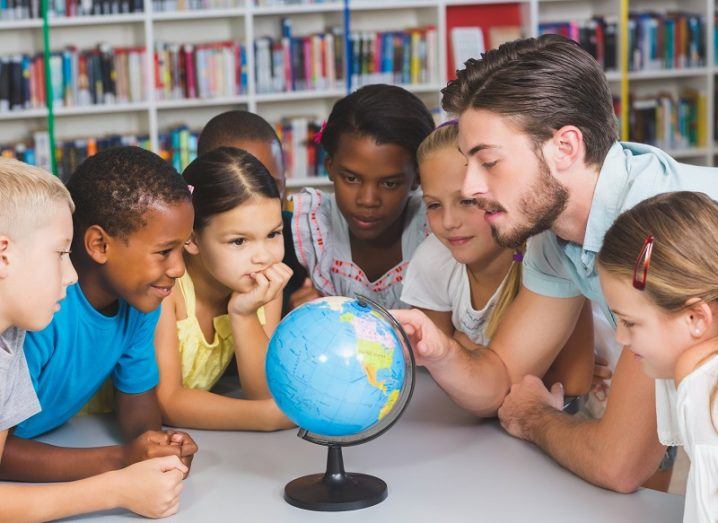 Young children of different ethnicity and a teacher gathered around a globe in a classroom.