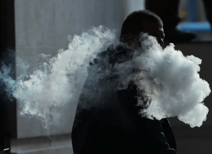 The silhouette of a man vaping on a public street. There is a cloud of smoke around his shadow.