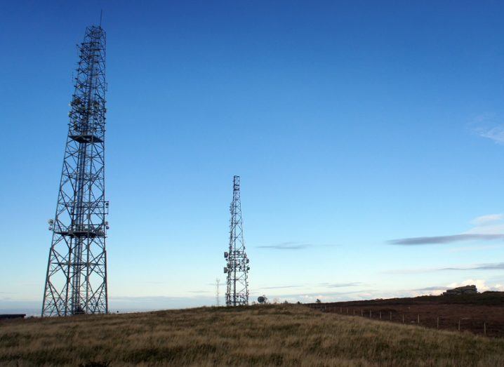 Two mobile network masts in a rural area against a dusk sky.