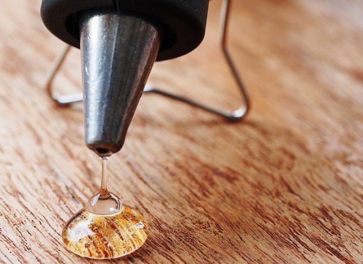 Close-up of a glue gun putting glue on a piece of wood.