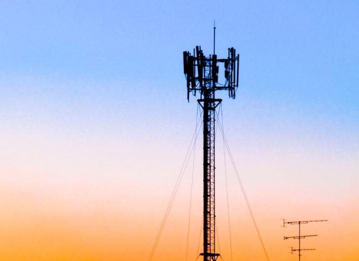 Silhouette of cellular tower against blue, pink and orange sunset sky.
