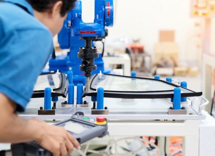 Person in a blue shirt using a device to control advanced manufacturing equipment in a factory.