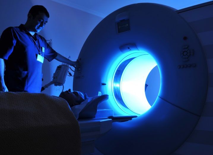 A doctor putting a patient into an MRI scanner emitting a blue light.