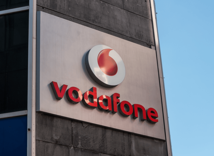 A grey building with the red Vodafone logo on the front. There is a blue sky in the background.