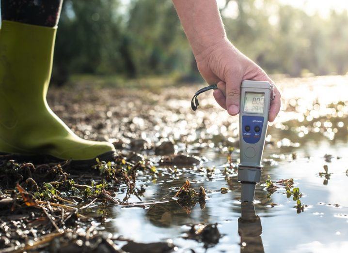 Person wearing green wellies placing a Ph monitoring device into a river.
