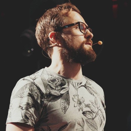 A man wearing a floral-patterned grey T-shirt presenting on stage.