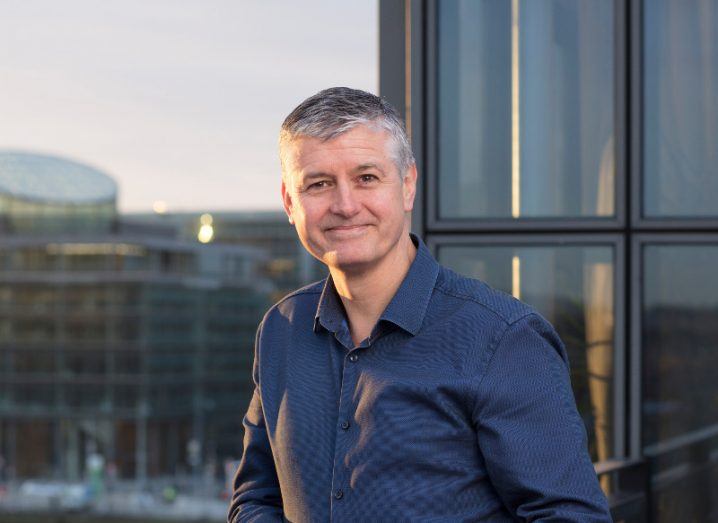 A man in a blue shirt stands outside at dusk, at a building overlooking Dublin city.