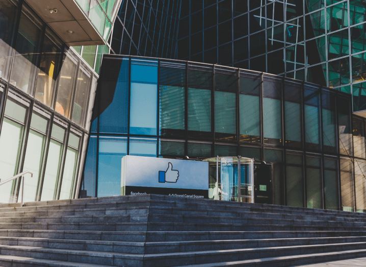 A set of concrete steps leading up to the entrance to Facebook's Dublin office, which is a glass building. Outside the door, there is a small billboard displaying Facebook's thumbs up logo.