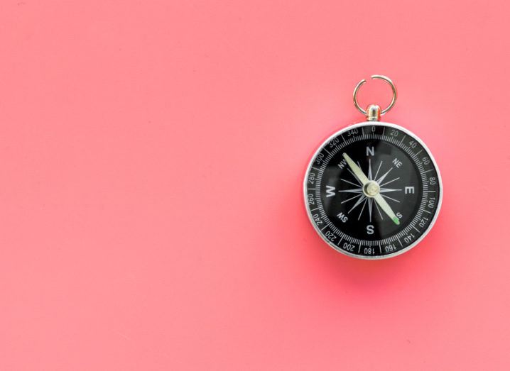 A black compass sits on a bright pink background.