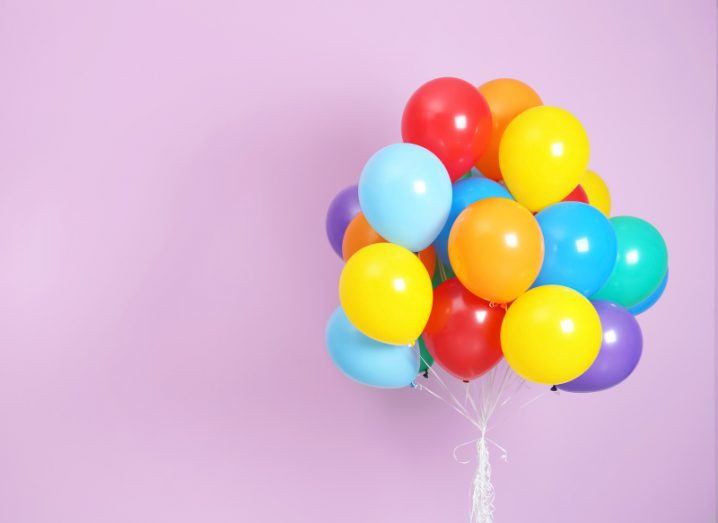 A colourful bunch of balloons gathered up against a dusky pink background.