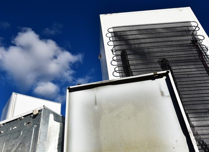 Towering, damaged refrigerators against a blue sky with clouds.