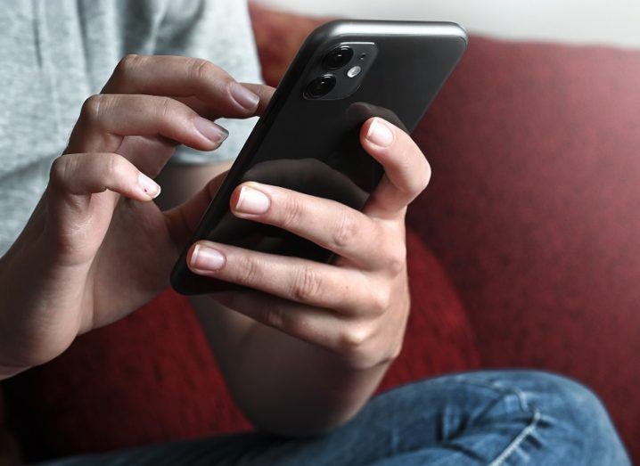 Hands of a person holding a mobile phone while sitting on a red couch.