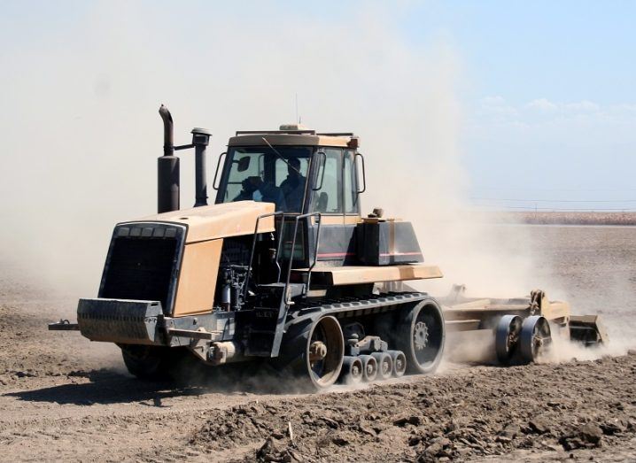 Large, orange tractor tilling dry, dusty land.