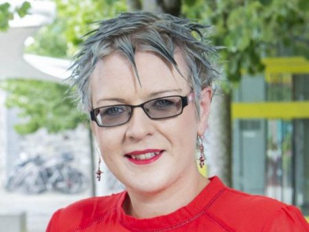 Caroline O'Driscoll is smiling into the camera in an outdoor setting, wearing a bright red dress.