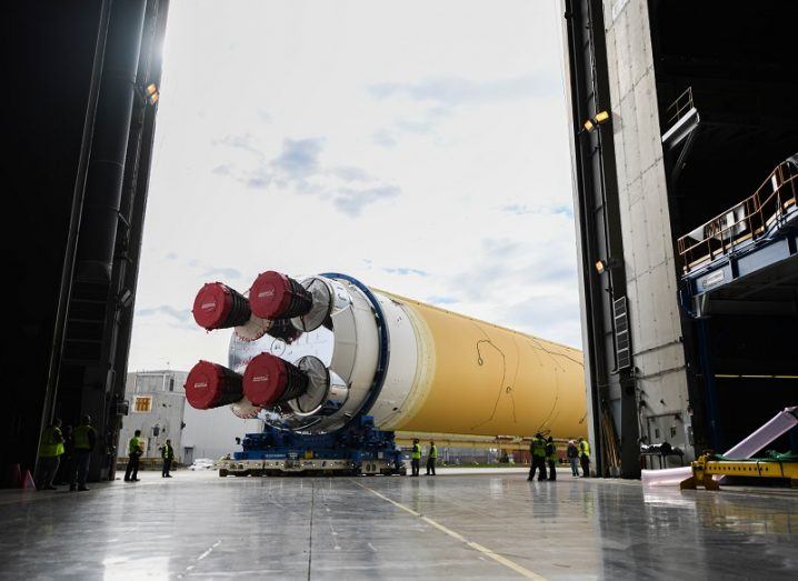 NASA's massive Space Launch System rocket being rolled out of a hangar against a sunny sky background.