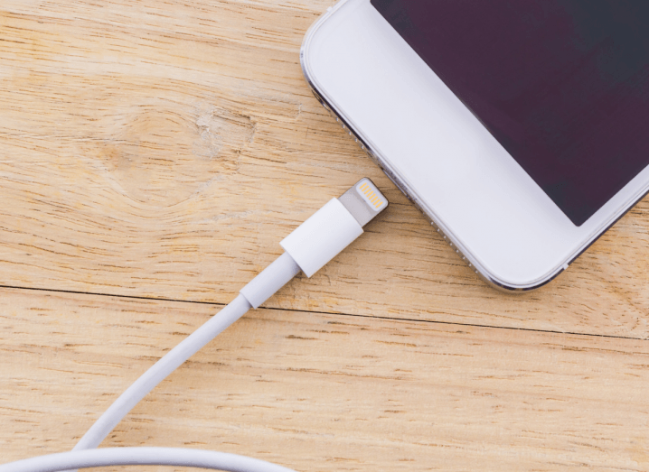 A white Lightning cable plugged into an iPhone 5.