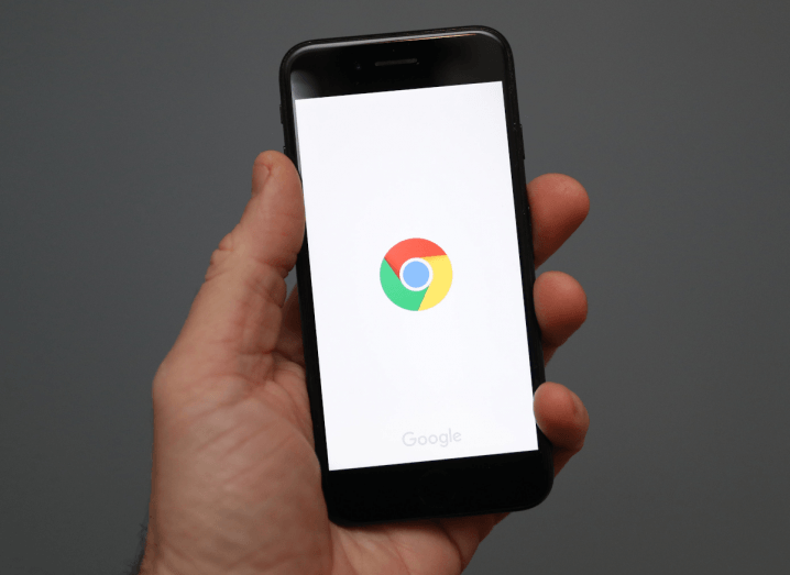 A hand holding an iPhone that is loading Google Chrome.
