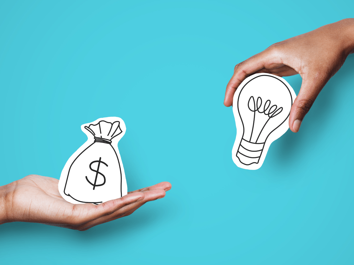 Two hands are edging into frame against a bright blue background. One hand is holding a drawing of a bag with a dollar sign on it, the other hand is holding a drawing of a lightbulb.