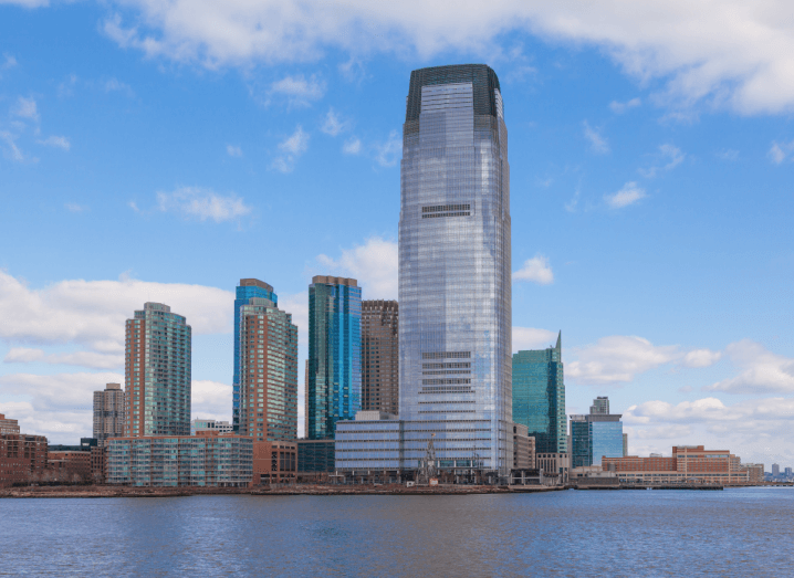A large skyscraper towering over other buildings in front of a body of water.