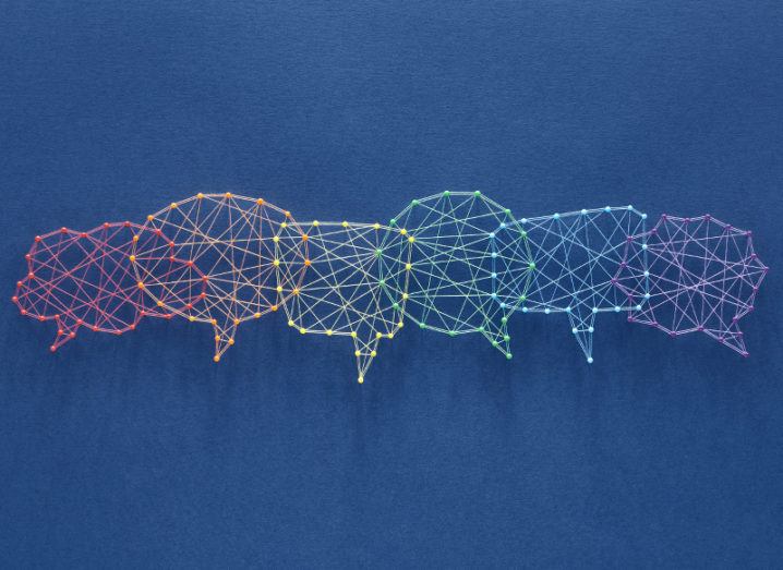 Colourful threads are wound around pins on a blue board, forming the shape of interconnecting speech bubbles symbolising comments on social media.