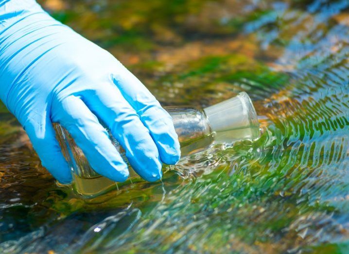 Blue surgical glove holding a beaker within a pool of water.