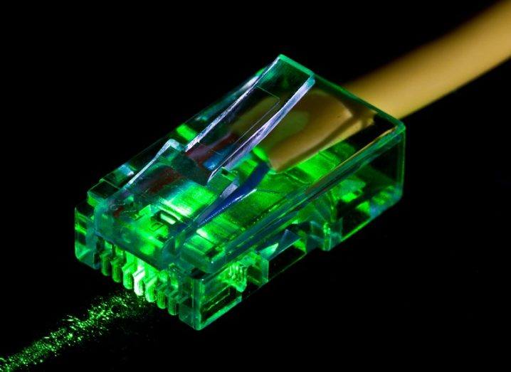 A yellow ethernet cable lit up by green laser light against a black background.