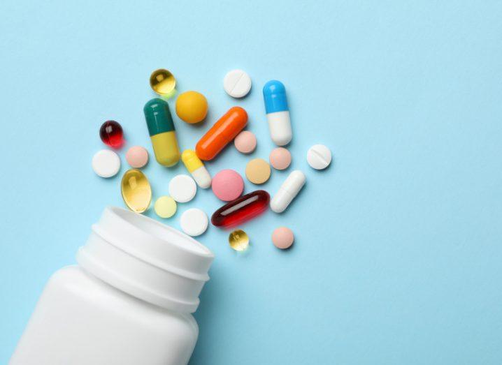 An open pill bottle lying on a bright blue background with an assortment of antibiotics scattered around.