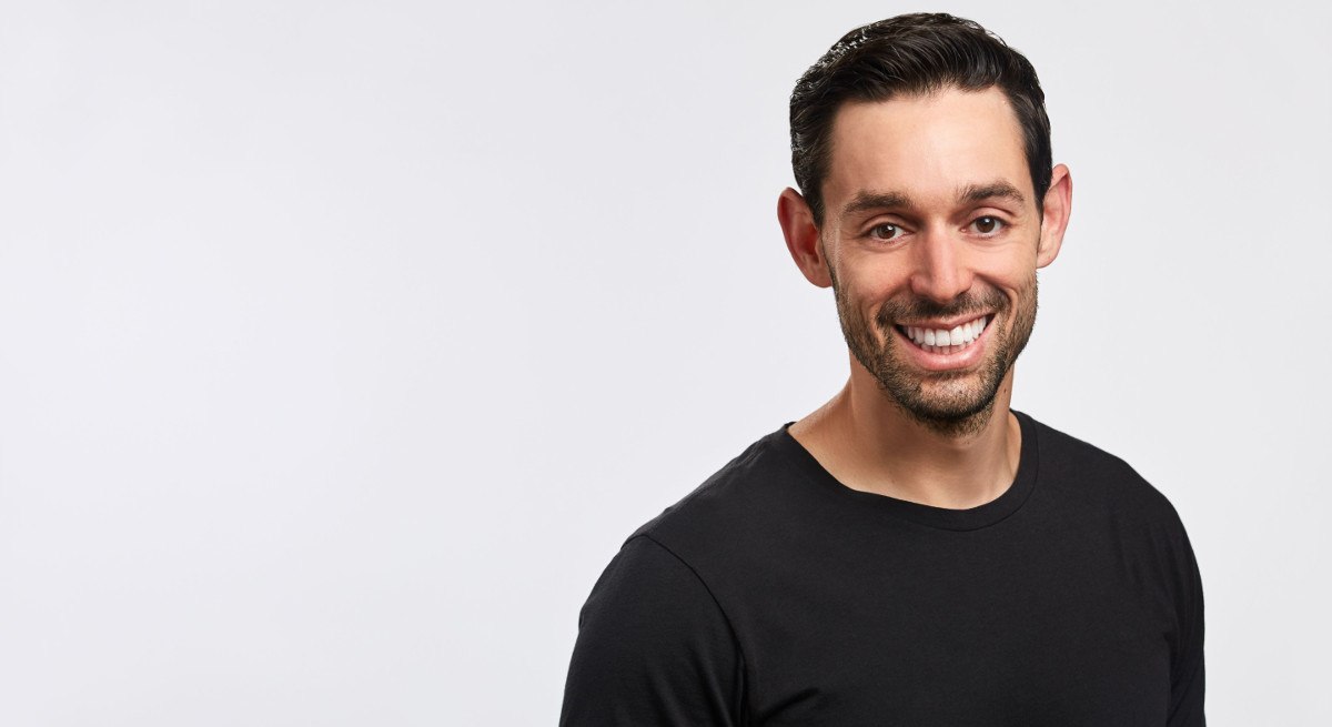 Jacob Morgan is smiling into the camera, wearing a black t-shirt and standing in front of a white background.