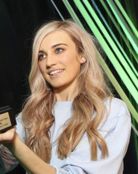 Niamh Donnelly, a young woman with long blonde hair, is pictured receiving an award on stage.