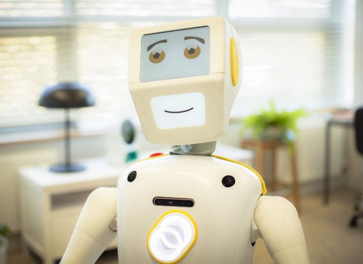 A robot with a screen displaying eyes and mouth in a relaxed setting is pictured in a residential elder care setting.