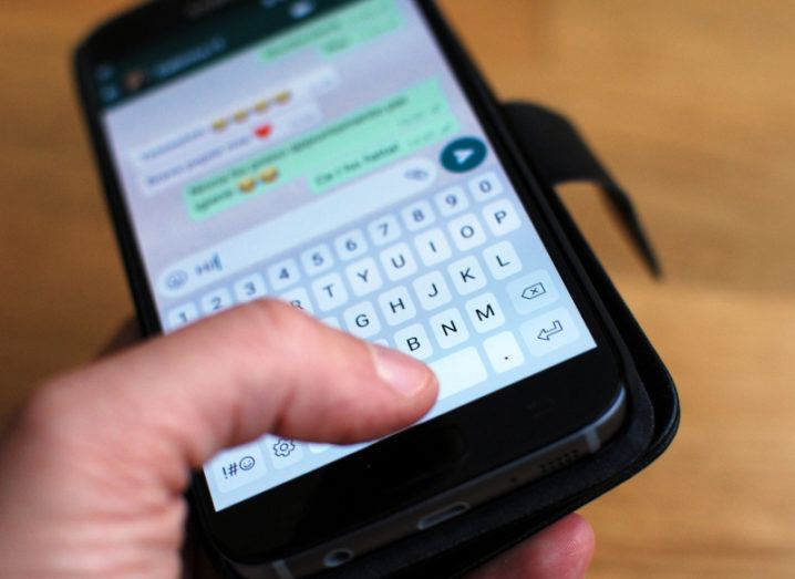 Hand holding a black smartphone with screen out of focus showing an open WhatsApp conversation.