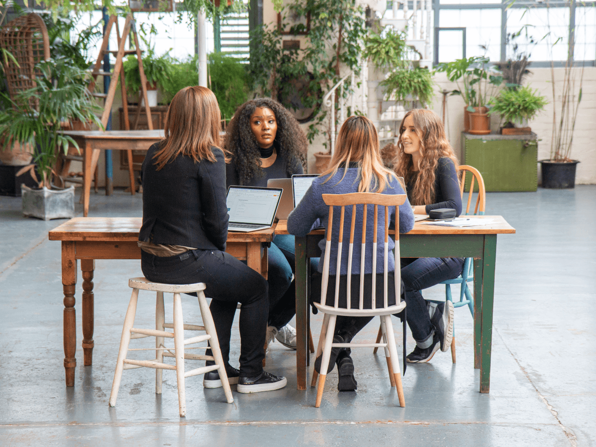 Women sitting at a desk in a bright room with lots of potted plants.