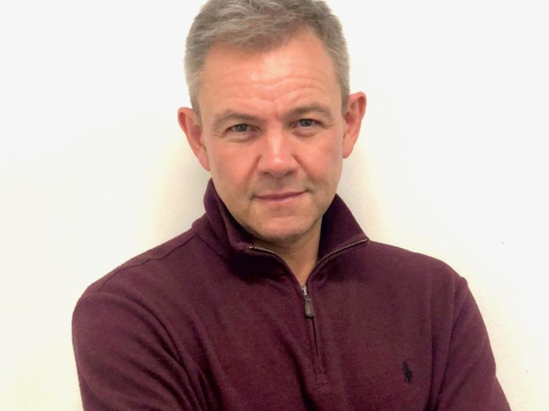 A close-up image of a man in a purple jumper.