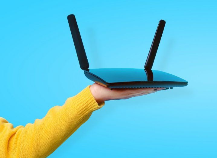 A yellow-jumpered arm is holding up a wi-fi router against a bright blue background.