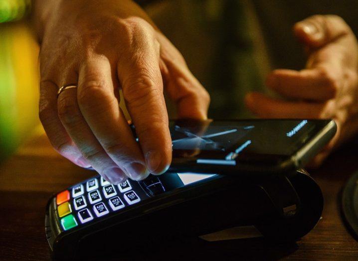 Hand of a person using a contactless payment machine with their phone.