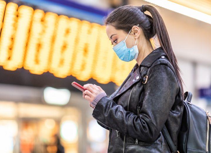 Woman in a leather jacket wearing a face mask at an airport and checking her phone.