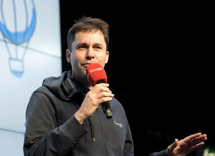 Nick Leeder holding a red microphone on stage at a Google event.