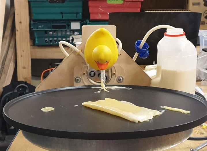 Science Hack Day project. A rubber duck is facing down at a large metal black plate. There is a plastic jug of pancake mix hooked up to the duck.