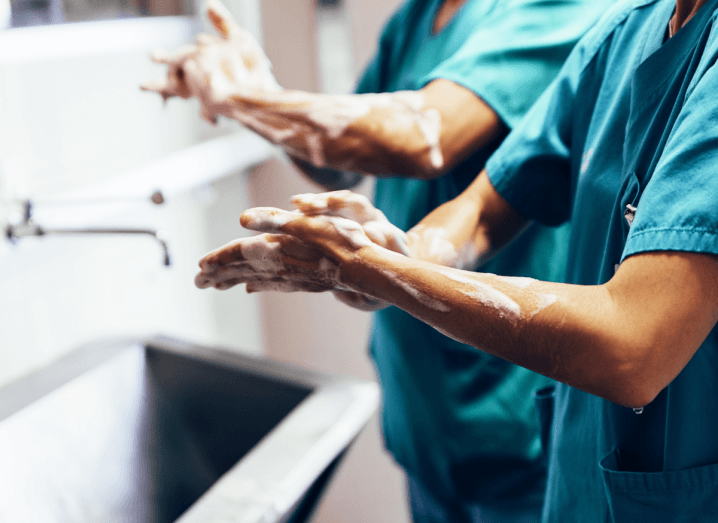 Two medical professionals wearing scrubs standing in front of a sink washing their hands with soapy water.