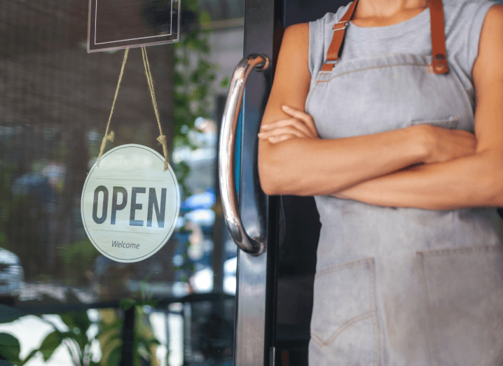 A woman wearing an apron standing outside the door of a business.