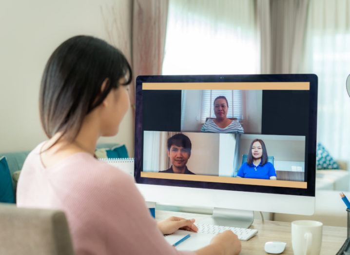 A shot of a woman sitting at a desk staring at a computer screen and having a Zoom call. There are three other faces on the call.